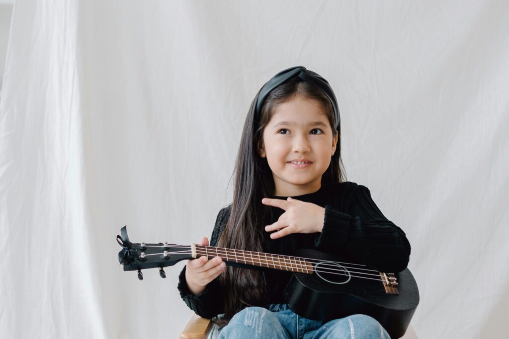Adorable young girl in studio playing a ukulele with a cheerful expression.